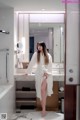 A woman in a white robe standing in a bathroom.