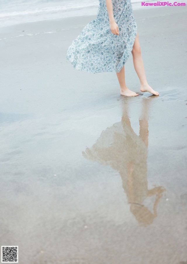 A woman in a blue dress walking on the beach.