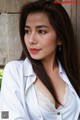 A woman in a white shirt leaning against a wall.