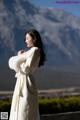 A woman in a white coat standing in front of a mountain.