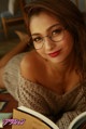 A woman wearing glasses laying on a couch reading a book.