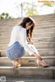 A woman in a white shirt and blue jeans crouching down on some steps.